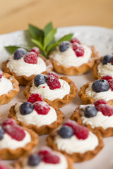 Homemade tartlets with vanilla cream and organic blueberries and raspberries decorated with mint on white plate. Delicious sweet dessert for party or celebration.