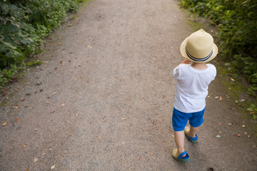 Top view on cite little toddler boy in straw hat walking on the countryside road on sunset. Lifestyle concept