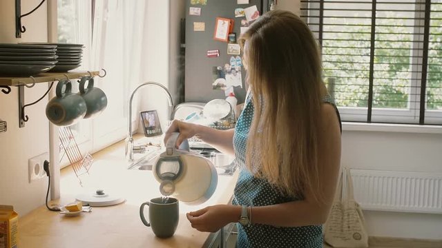 Young happy mother pouring hot water in the mug to make a cup of tea. Slow mo, Steadicam shot
