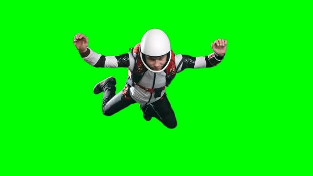 Slow motion video of calm professional skydiver performing free fall, counting meters till parachute opening time and looking at altimeter on his wrist against green background, chroma key