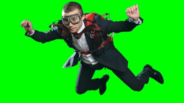 Slow motion footage of business man wearing parachute, formal suit and aviator mask, flying in mid air experiencing free fall looking calm and confident, chroma key against green screen background