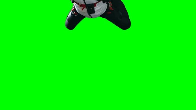 Locked down shot of skydiver man in helmet and parachuting gear gliding down slowly from above against green background, chroma-key, extreme sports concept