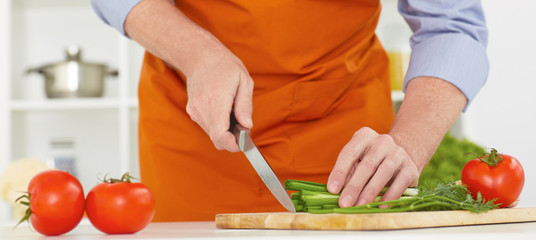 Mid section of a man with a knife cuting green onion on the kitchen background.