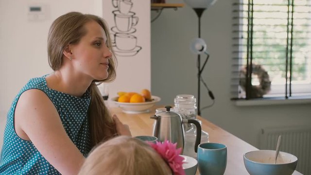A close-up of a beautiful young mother and her daughter who is colouring at the kitchen table. Slow mo, Steadicam shot