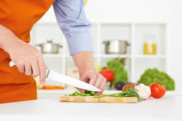Closeup man's hand with a knife cutting green onion on a wodden board.