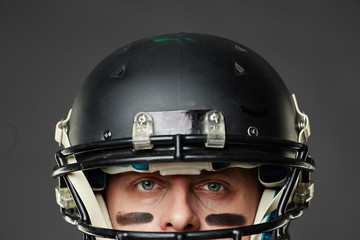 Isolated on black background closeup of head of blue-eyed man with eye black wearing football...
