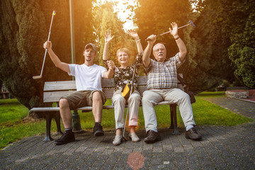 Zwei Generationen einer Familie sitzen auf einer Parkbank. Sie geben ihrer Freude mit Jubel Ausdruck. Die Sonne im Hintergrund erhellt die Szene durch die Bäume.