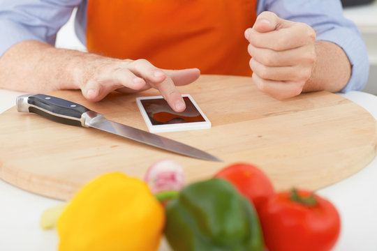 Cooking, technology and home concept - closeup of man pointing finger to smartphone.