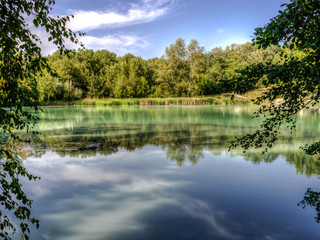 Fototapeta na wymiar Hydrogen sulphide lake landscape with turquoise water in tree branches framing with forest reflection.
