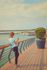Fototapeta premium Girl using cellphone on the pier near the river.