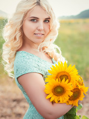 Portrait of a beautiful smiling blonde girl outdoors with sunflowers in hands on a rainy day in sunset