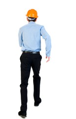 Back view of running engineer in helmet. Businessman in a blue shirt and a helmet in an emergency.