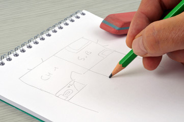 Homme dessinant le plan d'une maison au crayon à papier sur un bloc-notes à spirales