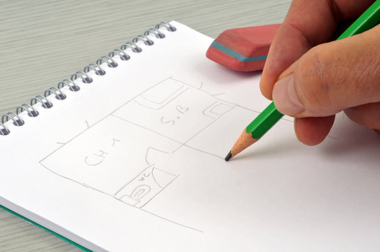Homme dessinant le plan d'une maison au crayon &agrave; papier sur un bloc-notes &agrave; spirales