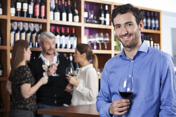 Smiling Man Holding Wineglass While Friends Standing In Backgrou