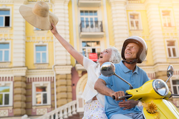 Man on scooter is smiling. Hat in woman's hand. Our dream came true. Happiness without bounds.