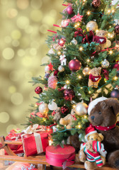 Beautiful decorated Christmas tree with sparkling  lights, baubles, teddy bears and red gifts.
Defocused gold bokeh background.
