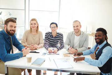 Group of businesspeople, men and women, pausing discussion to look and smile at camera during meeting in office