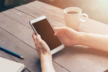 Woman hand holding phone and using phone on table in garden at c