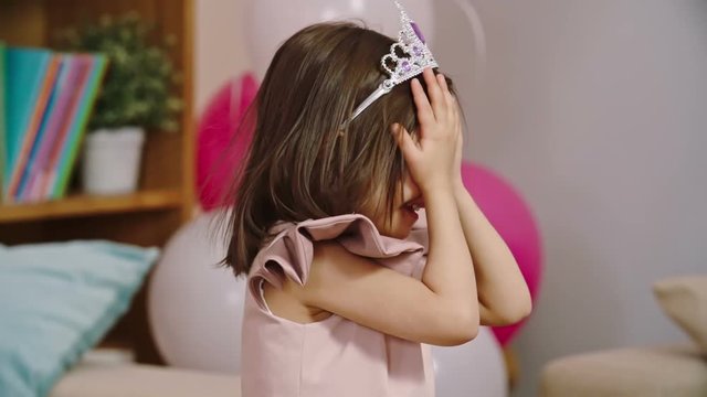 Little girl wearing diamond tiara covering her eyes with hands while playing hide and seek game