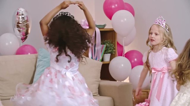 Beautiful little girls in princess crowns and dresses dancing like ballerinas during birthday party at home