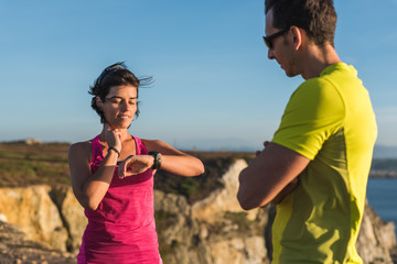 Fitness runner woman checking heart rate pulse with watch and trainer during outdoor trail running workout. Couple team doing intensity workout outside together training.