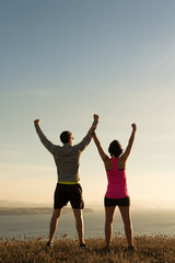 Sporty runner couple rising arms in victory sign after successful training outdoor on the coast...