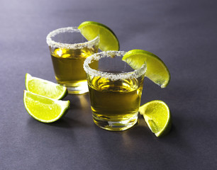 Gold tequila with lime and salt on dark table
