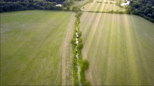 Aerial shot of stream in the fields. Rays of sun shining from above.