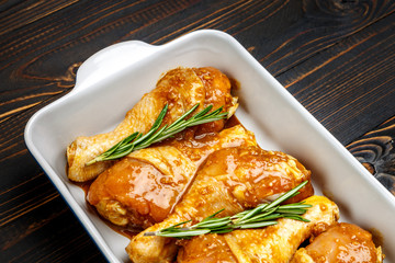 Raw chicken legs in baking dish on a wooden background