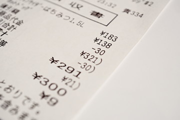 Macro detail of a Japanese paper receipt (white paper bill, sales slip) with a sum of several items and the additional tax as a symbol of market and accountancy in Japan