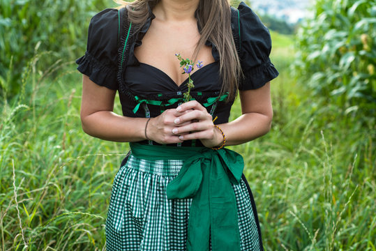 Junge Frau mit sch&ouml;nem Dekolletee im Trachtenkleid h&auml;lt Blume vor der Brust