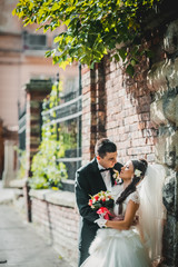 Obraz premium Handsome groom hugging beautiful bride with bouquet in romantic european park