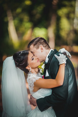 Handsome groom hugging beautiful bride with bouquet in romantic european park
