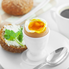 Perfect soft boiled egg, open bread sandwich with butter and cup of coffee on a table. Traditional food for healthy breakfast.