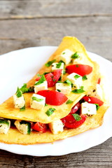 Omelet with cheese, tomatoes and parsley on a plate on old wooden background. Stuffed omelet recipe. Closeup