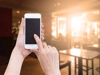 Hand holding blank screen mobile phone with blur coffee shop bac