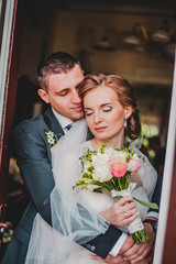 Bride and groom in a luxurious room in retro style. The rich young couple of man in suits and woman in vintage wedding dress. People on the stairs.