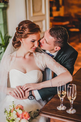 Bride and groom in a luxurious room in retro style. The rich young couple of man in suits and woman in vintage wedding dress. People on the stairs.