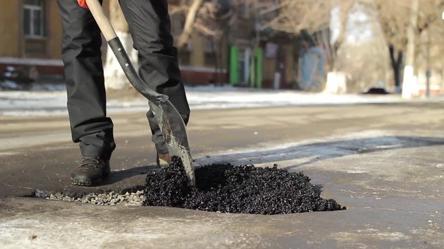 Filling up a pothole on road with cold asphalt by using shovel