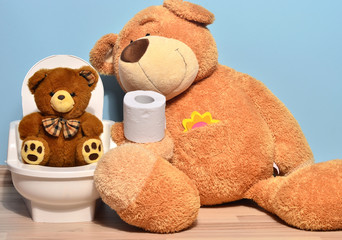 Small teddy bear sitting on the potty and playing with toilet paper, father bear teaching his cute kid how to pee and poo - obrazy, fototapety, plakaty