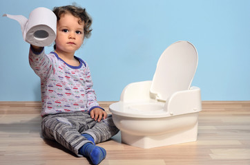 Baby toddler sitting near the potty and playing with toilet paper. Cute kid potty training for pee and poo - obrazy, fototapety, plakaty