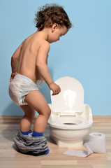 Baby toddler sitting near the potty and playing with toilet paper. Cute kid potty training for pee and poo - obrazy, fototapety, plakaty