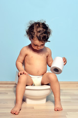 Baby toddler sitting on the potty and playing with toilet paper. Cute kid potty training for pee and poo - obrazy, fototapety, plakaty