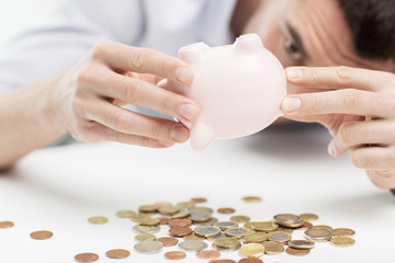 close up of man pouring coins from piggy bank