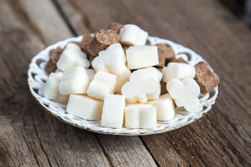 There is a figured brown and white sugar on a porcelain white saucer.There is a saucer on the  wooden surface.