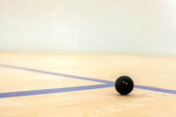 Black tennis ball with two yellow dots is lying on wooden court background - sport, fitness, healthy lifestyle and objects concept