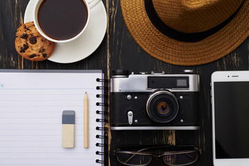 Close-up of notepad with pencil, eyeglasses, phone , hat, camera