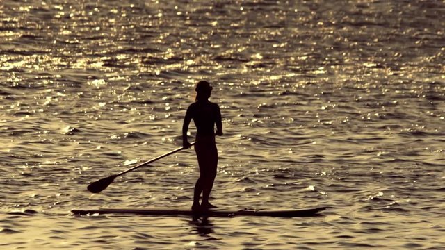 Woman silhouetted doing stand up paddle in the open sea at sunset 100p