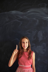 Young pretty girl standing and showing forefinger against blackb